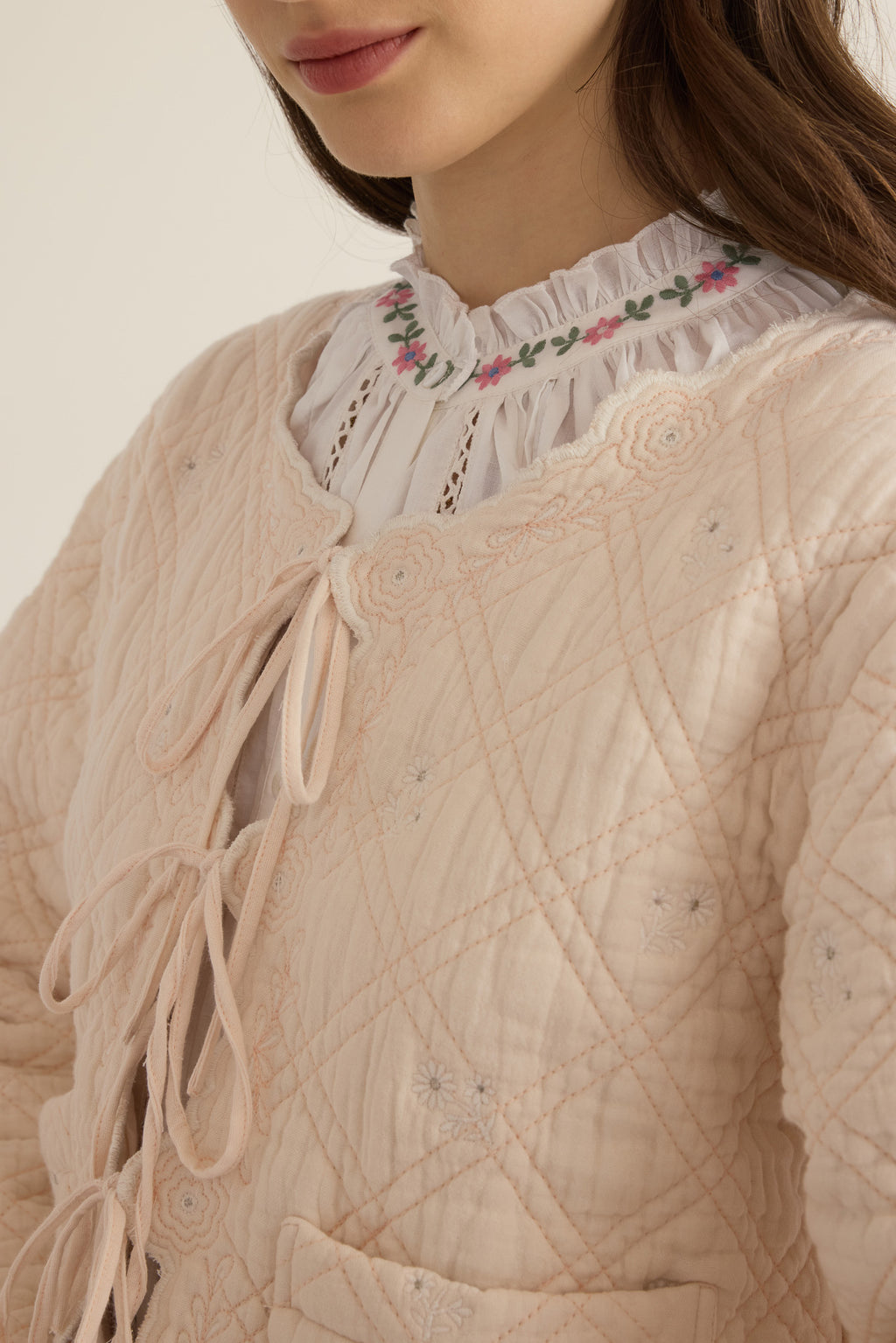 Front closeup view of front tie detail with floral scallop embroidery, model wearing the Anais Organic Cotton Quilted Jacket with Ties in rosewater pale pink