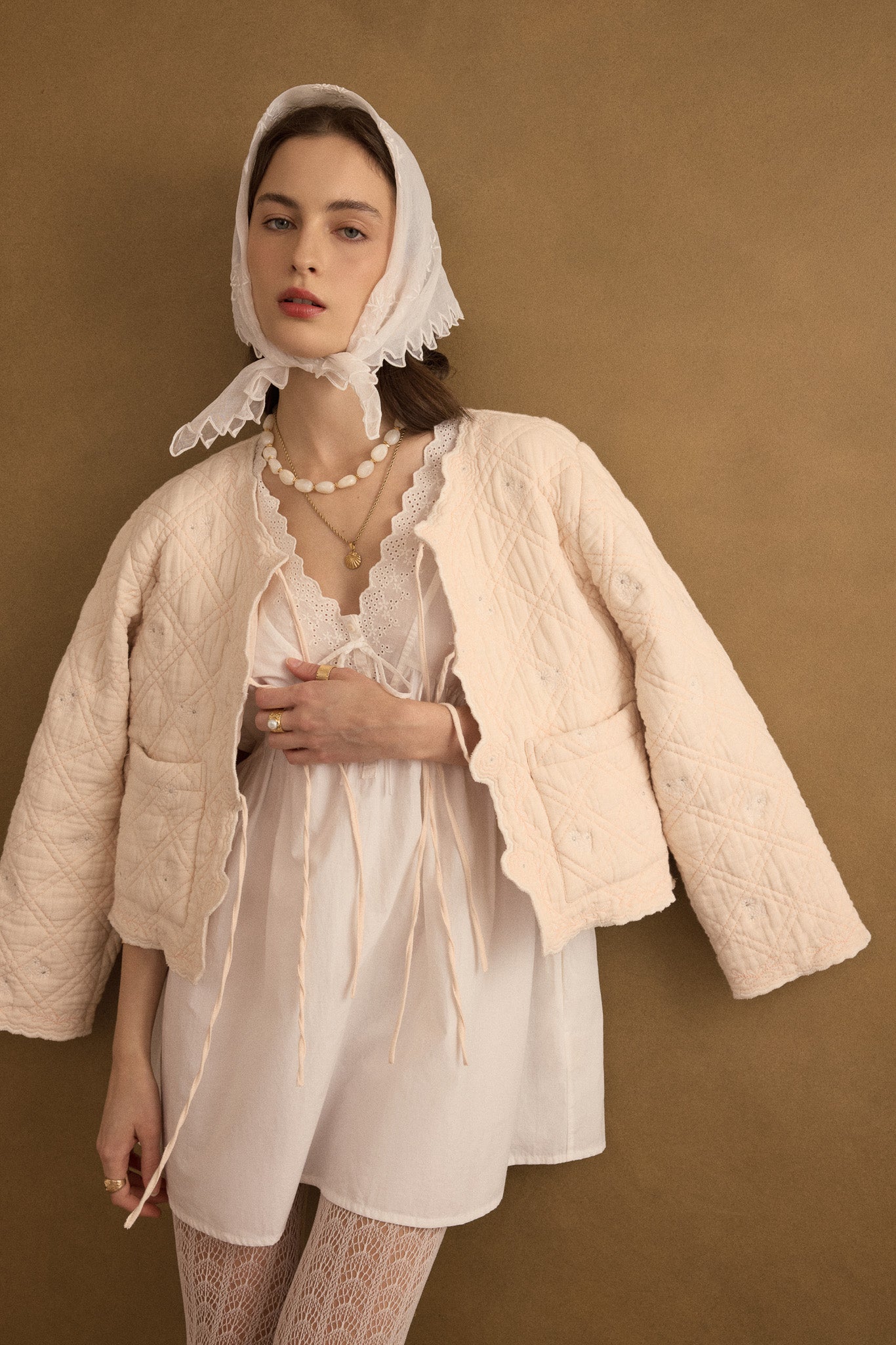 Editorial styling view of model wearing the Anais Organic Cotton Quilted Jacket with Ties in rosewater pale pink over the Amelie short dress in ivory