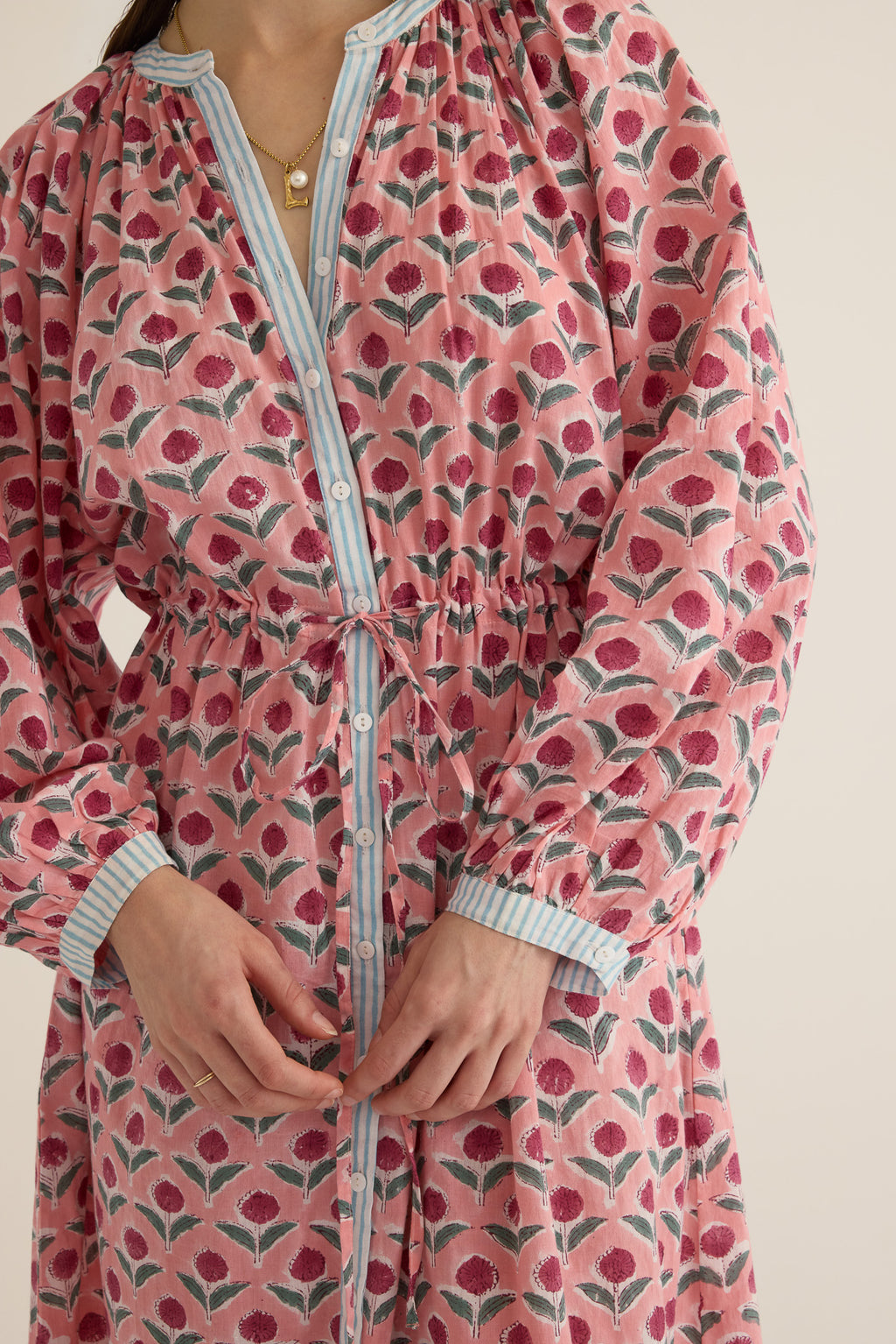 Front closeup view of model wearing the Juliet Block Printed Cotton Drop Sleeve Raglan Shirt Dress in Pink Dahlia, showing the mother of pearl buttoned front and waist tie