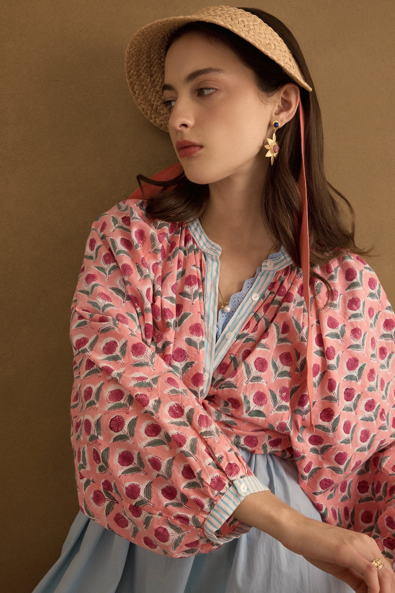 Editorial closeup view of model wearing the Juliet Block Printed Cotton Drop Sleeve Raglan Shirt in Pink Dahlia, styled with a raffia hat and statement gold semi precious stone earrings