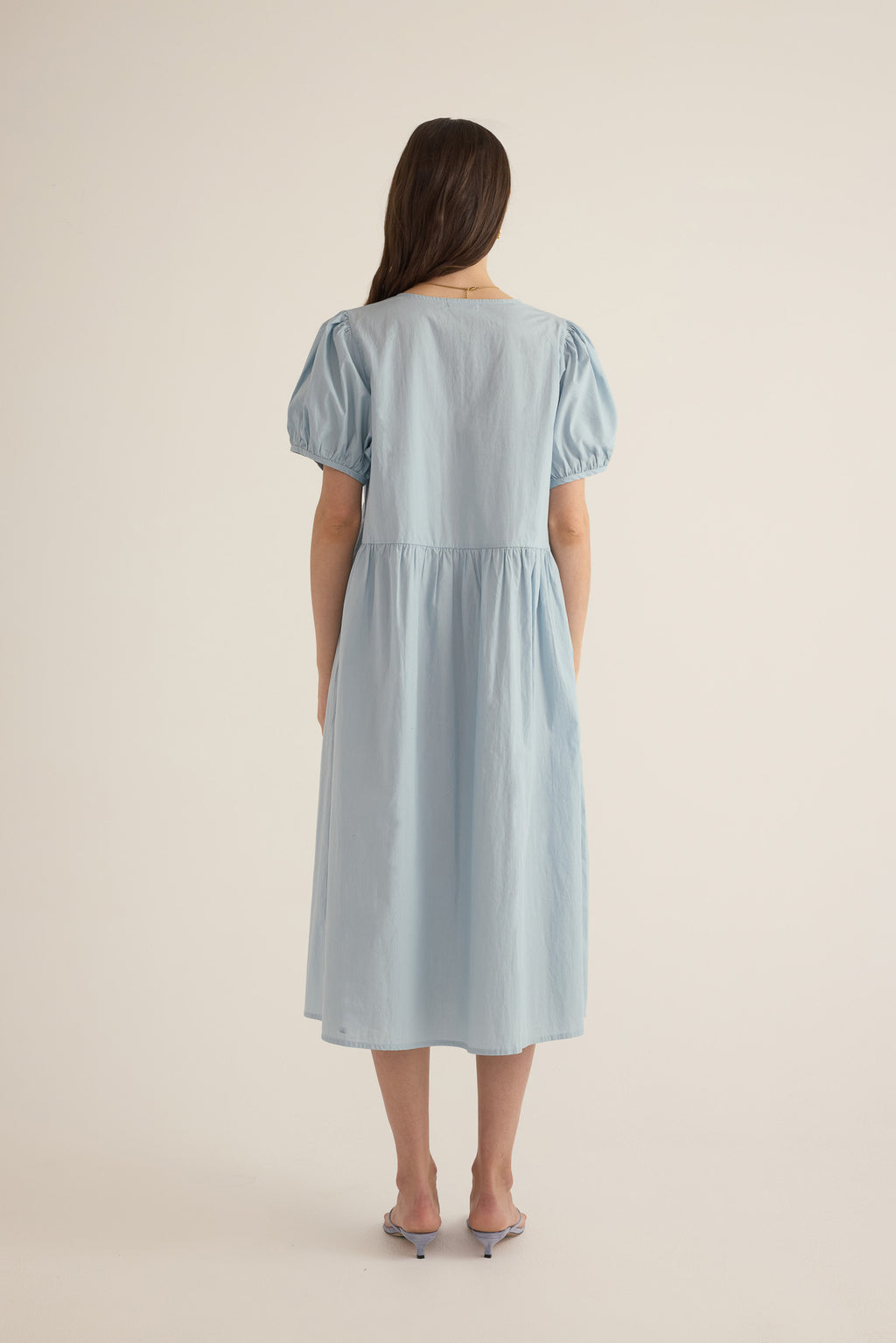 Back view of model wearing the Amelie organic cotton v-lace midi dress in forget me not pale blue.