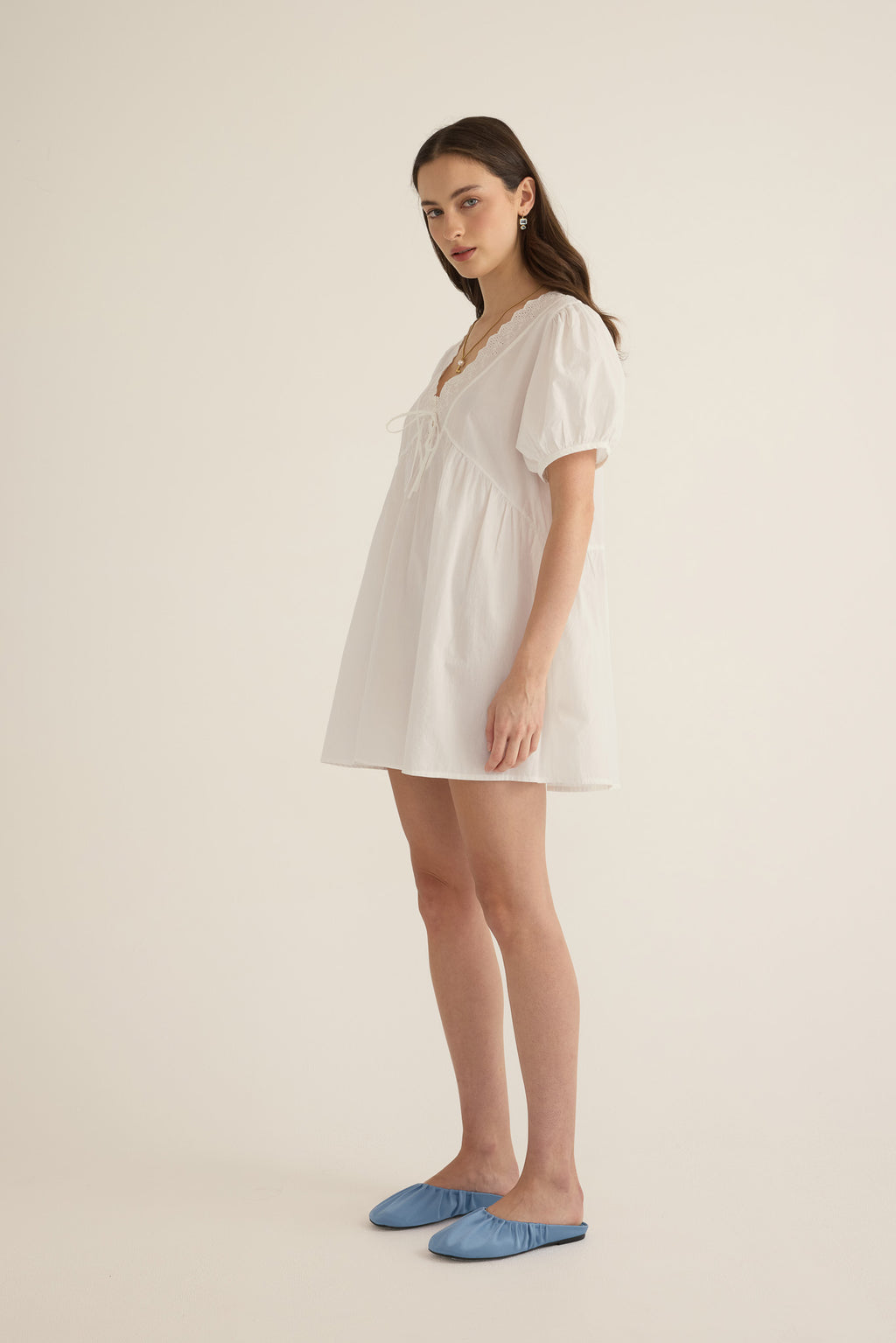 Side view of model wearing the Amelie organic cotton v-lace short dress in ivory.