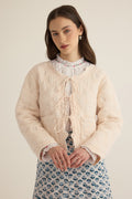 Front detail closeup view of model wearing the Anais Organic Cotton Quilted Jacket with Ties in rosewater pale pink, showing tie front and floral embroidery quilting detail