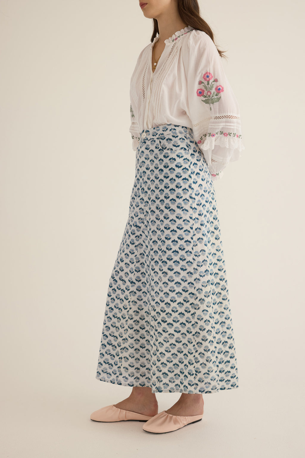 Front side view of model wearing the Joni Block Printed Cotton A-Line Midi Skirt in Blue Gardenia paired with the Juliet Embroidered Cotton Juliet Drop Sleeve Raglan Shirt in Ivory with floral embroidered motifs, pintucking and lace detail