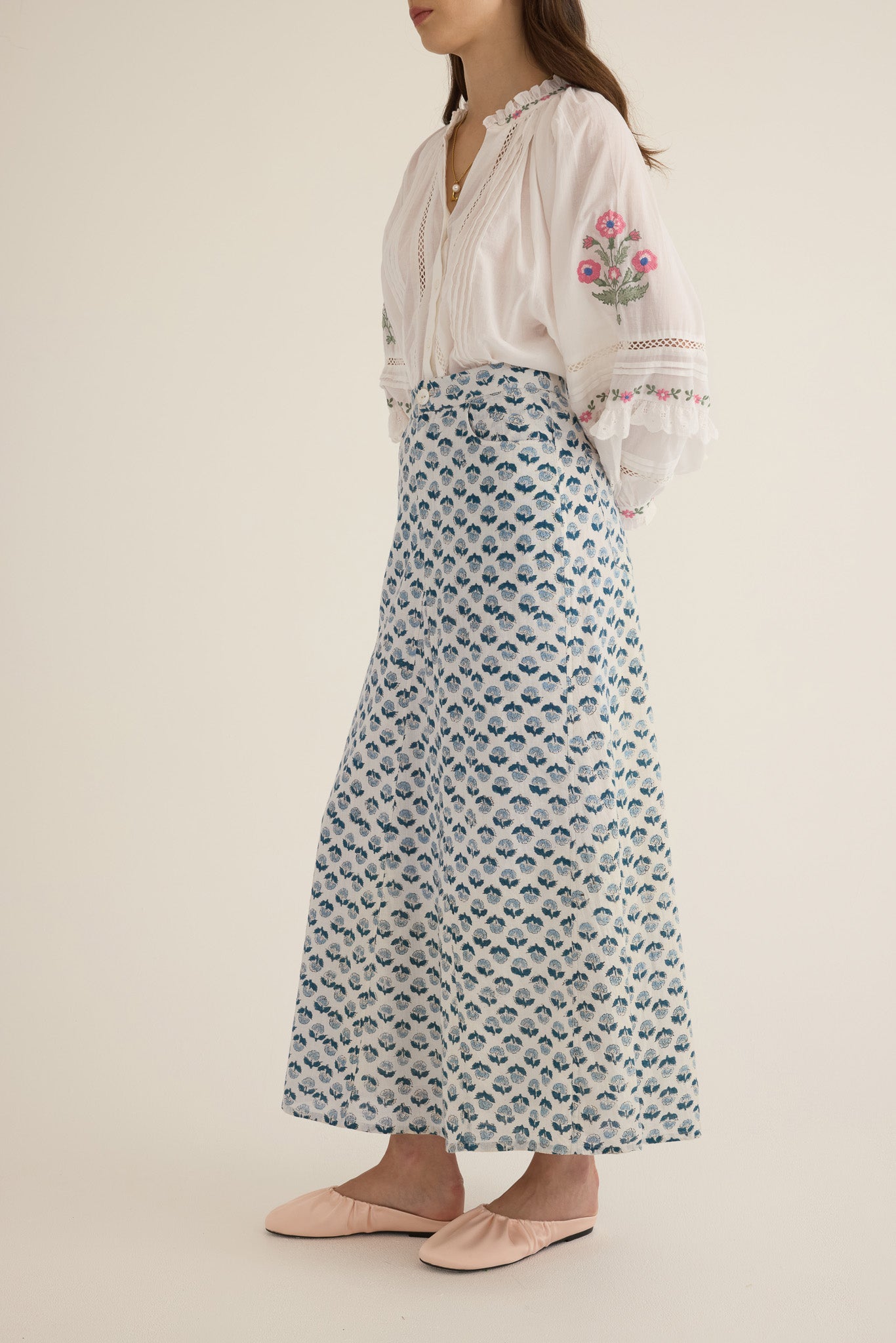 Front side view of model wearing the Joni Block Printed Cotton A-Line Midi Skirt in Blue Gardenia paired with the Juliet Embroidered Cotton Juliet Drop Sleeve Raglan Shirt in Ivory with floral embroidered motifs, pintucking and lace detail