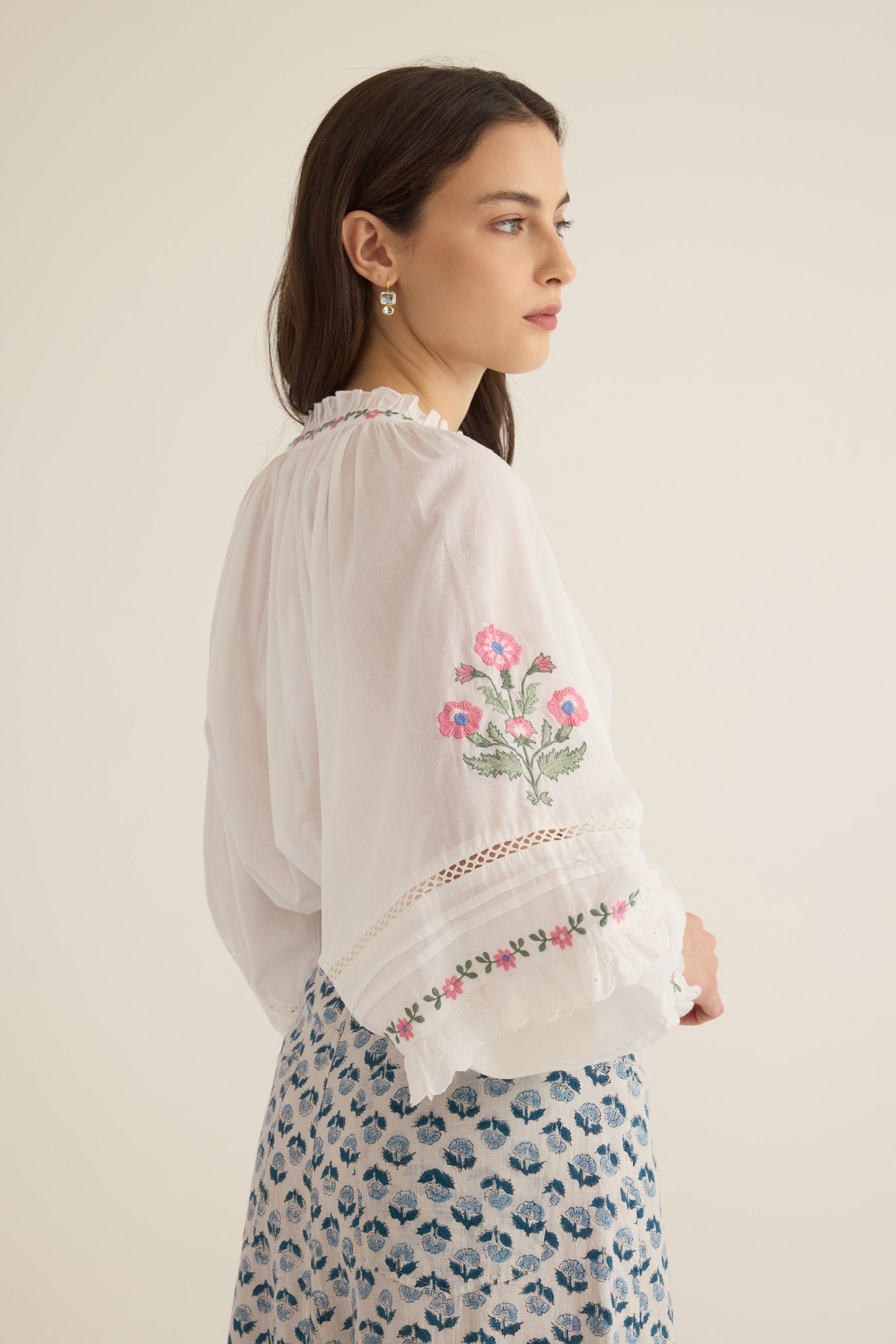 Side sleeve view of model with arms at hips wearing the Juliet Embroidered Cotton Juliet Drop Sleeve Raglan Shirt in Ivory with floral embroidered motifs, pintucking and lace detail, showing billowing sleeve detail