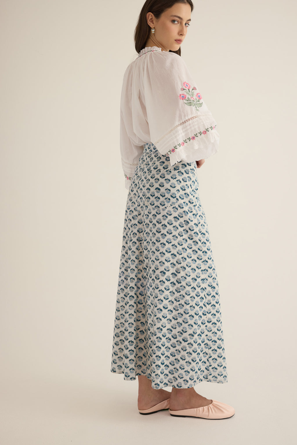 Side view of model wearing the Juliet Embroidered Cotton Juliet Drop Sleeve Raglan Shirt in Ivory with floral embroidered motifs, pintucking and lace detail, with the Joni A-Line Midi Skirt in Blue Gardenia blue handblock print