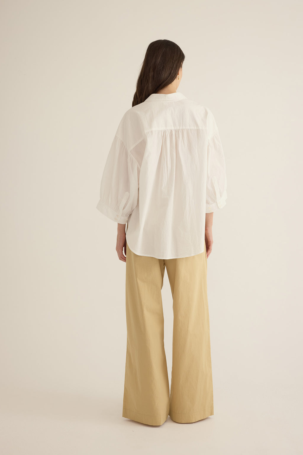 Back view of model wearing the Romeo wide-leg pleat pant in light beige organic cotton, styled with the Romeo wide cuff shirt in ivory