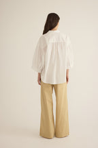 Back view of model wearing the Romeo wide-leg pleat pant in light beige organic cotton, styled with the Romeo wide cuff shirt in ivory