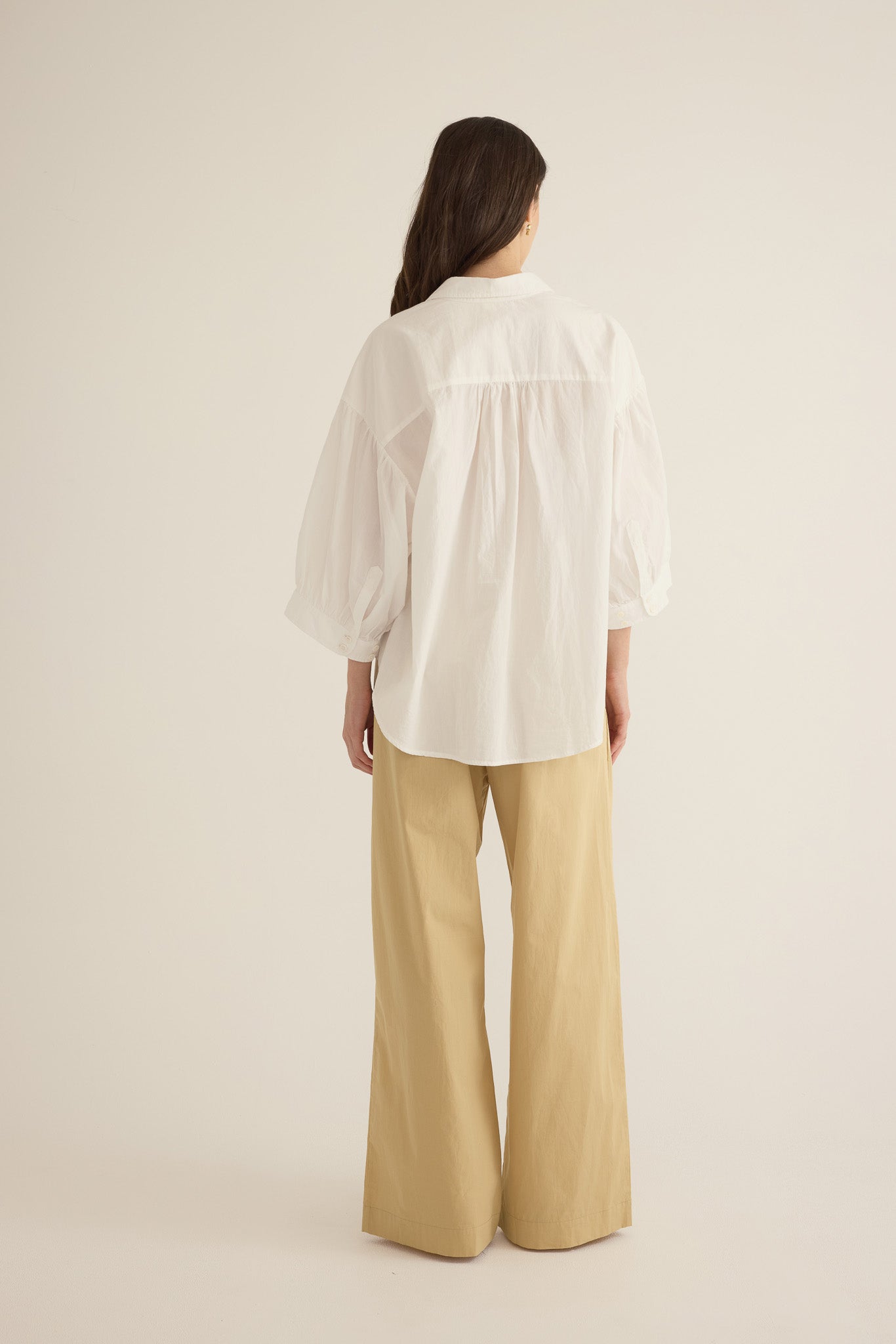 Back view of model wearing the Romeo wide-leg pleat pant in light beige organic cotton, styled with the Romeo wide cuff shirt in ivory