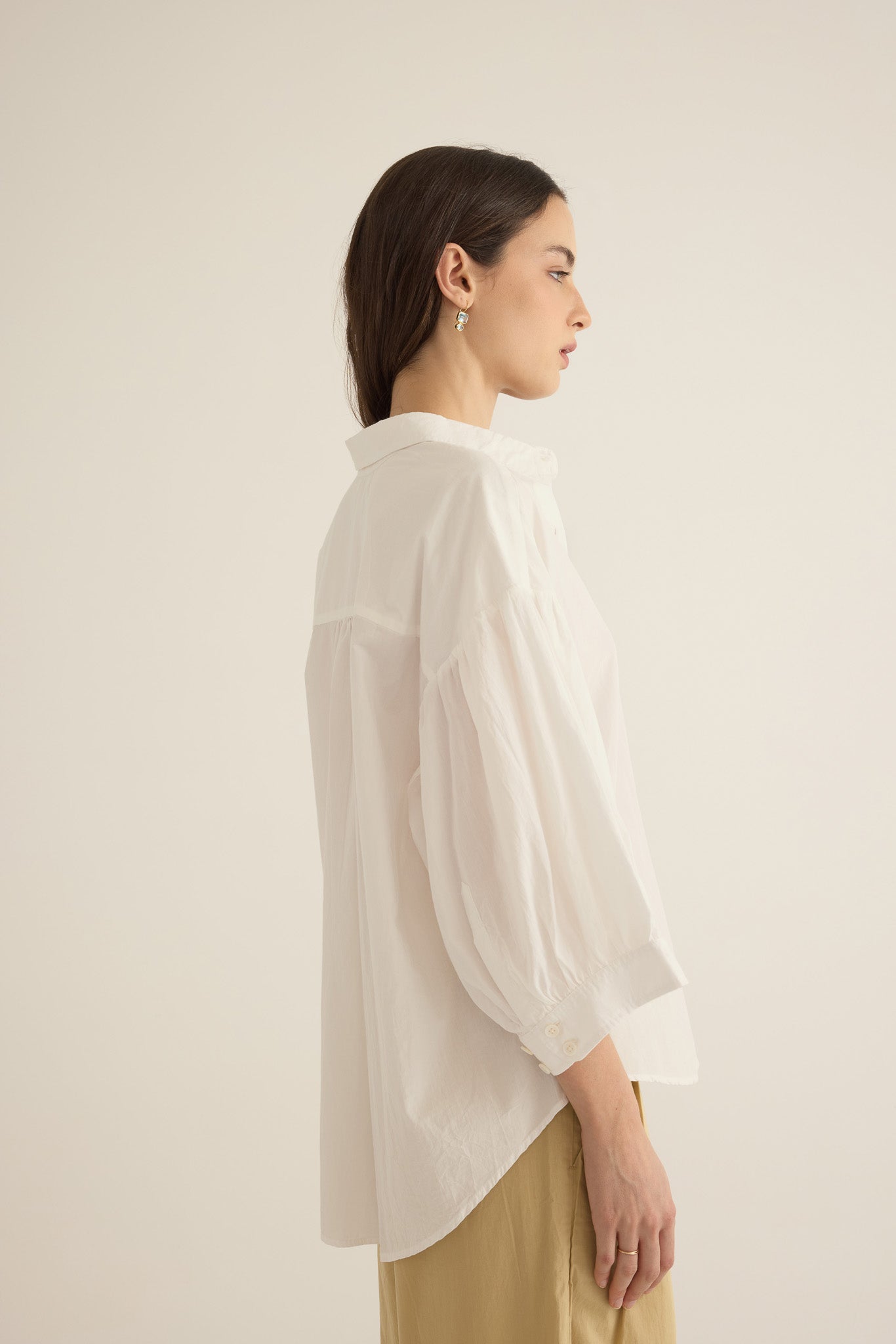 Side view of model wearing the Romeo wide-leg pleat pant in light beige organic cotton, styled with the Romeo wide cuff shirt in ivory