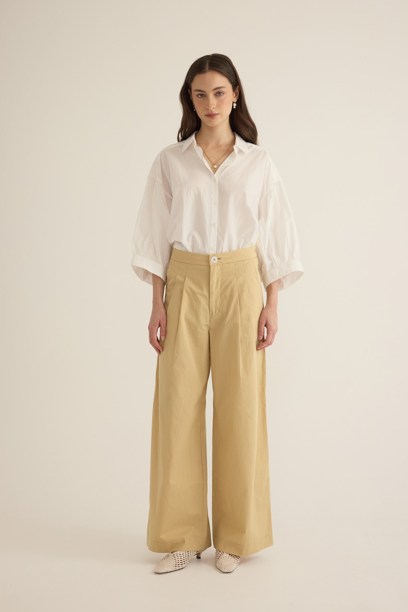 Side view of model wearing the Romeo wide-leg pleat pant in taos taupe light beige organic cotton, styled with the Romeo wide cuff shirt in ivory