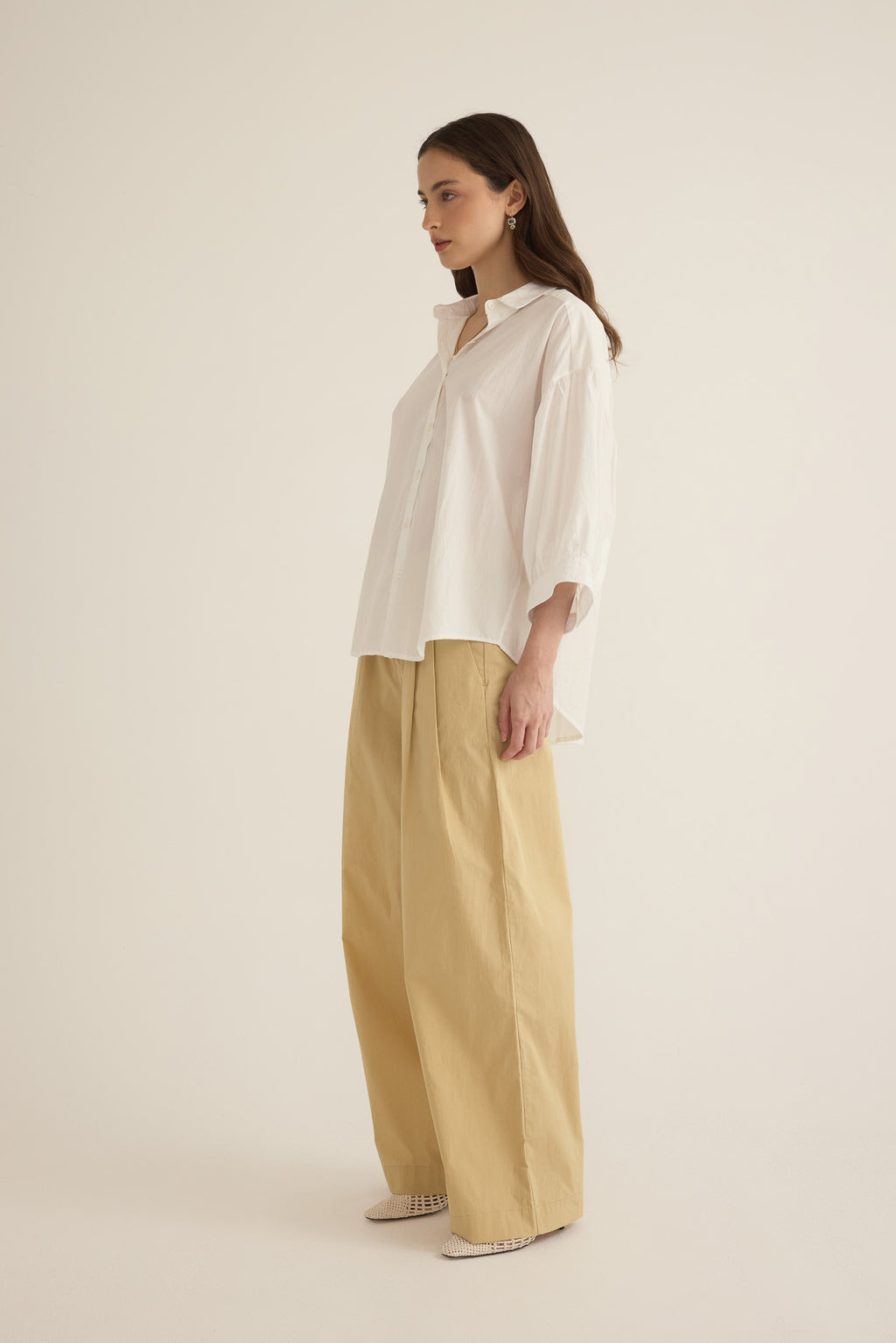 Side view of model wearing the Romeo wide-leg pleat pant in light beige organic cotton, styled with the Romeo wide cuff shirt in ivory