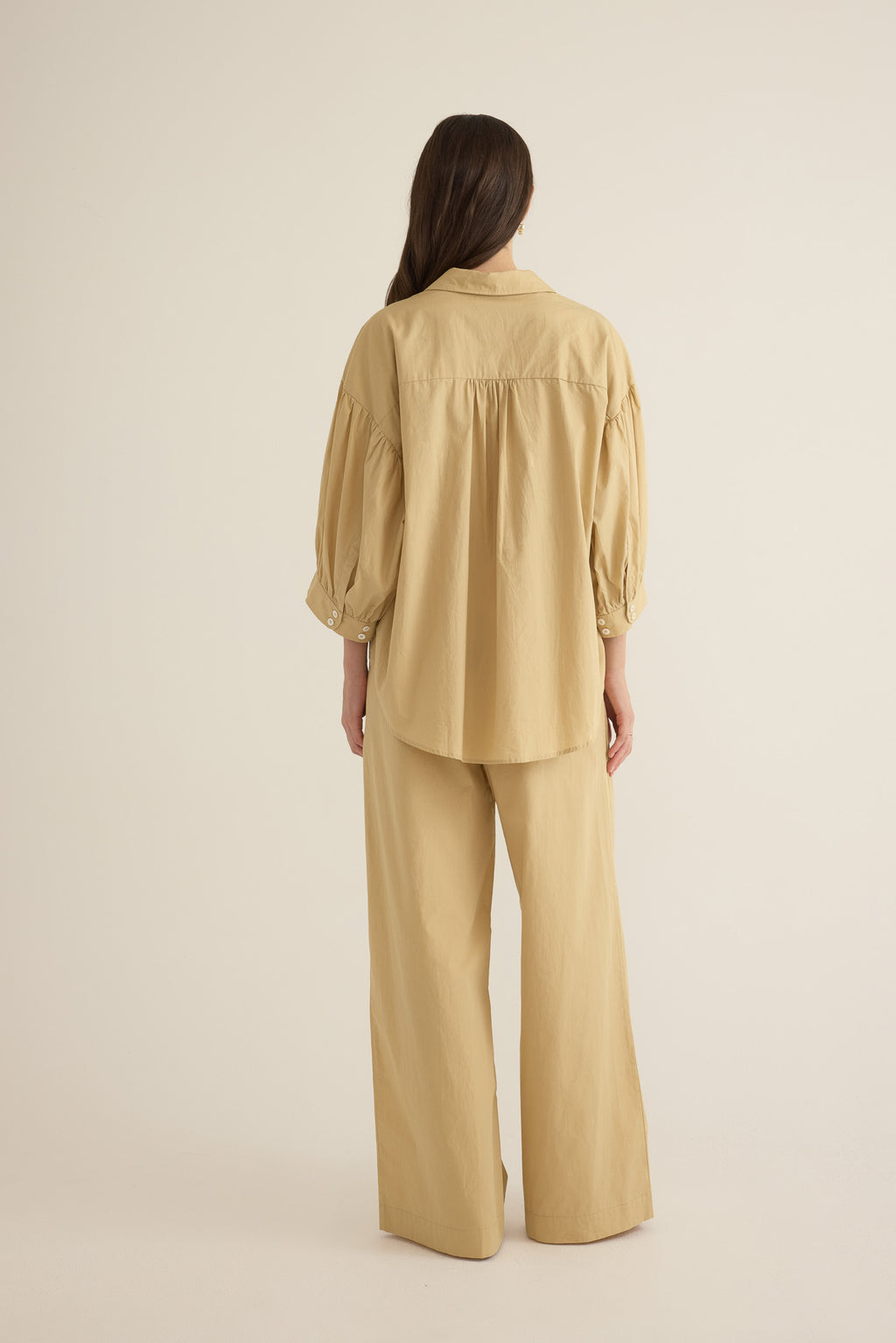 Back view of model wearing the Romeo wide-leg pleat pant in light beige organic cotton, styled with the Romeo wide cuff shirt in taos taupe beige