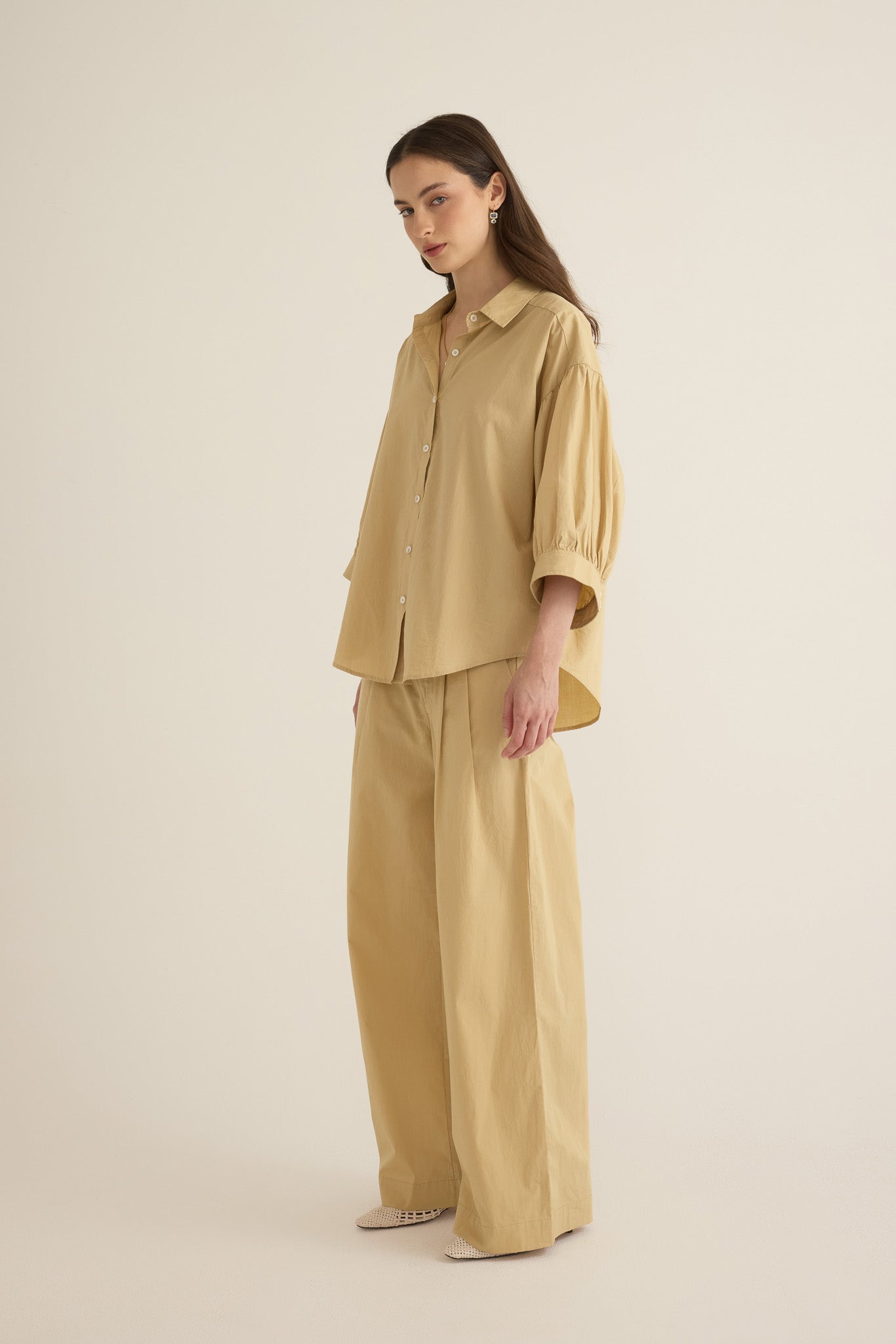 Side view of model wearing the Romeo wide-leg pleat pant in light beige organic cotton, styled with the Romeo wide cuff shirt in taos taupe beige