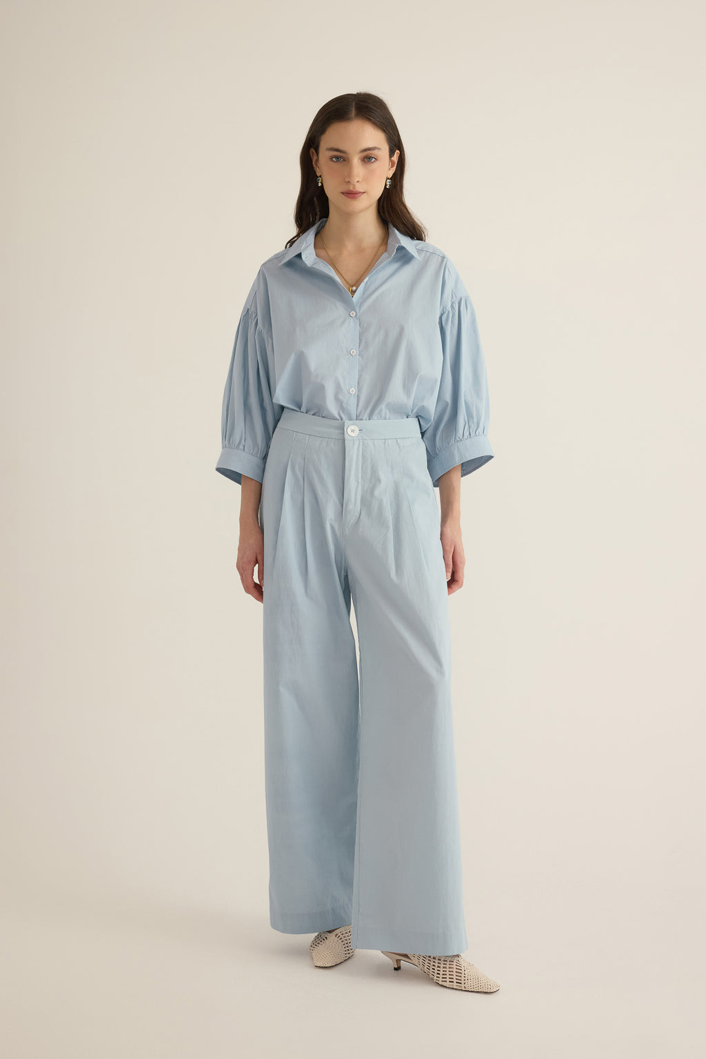 Font view of model wearing the Romeo wide-leg pleat pant in pale blue organic cotton, styled with the Romeo wide cuff blouson shirt in blue