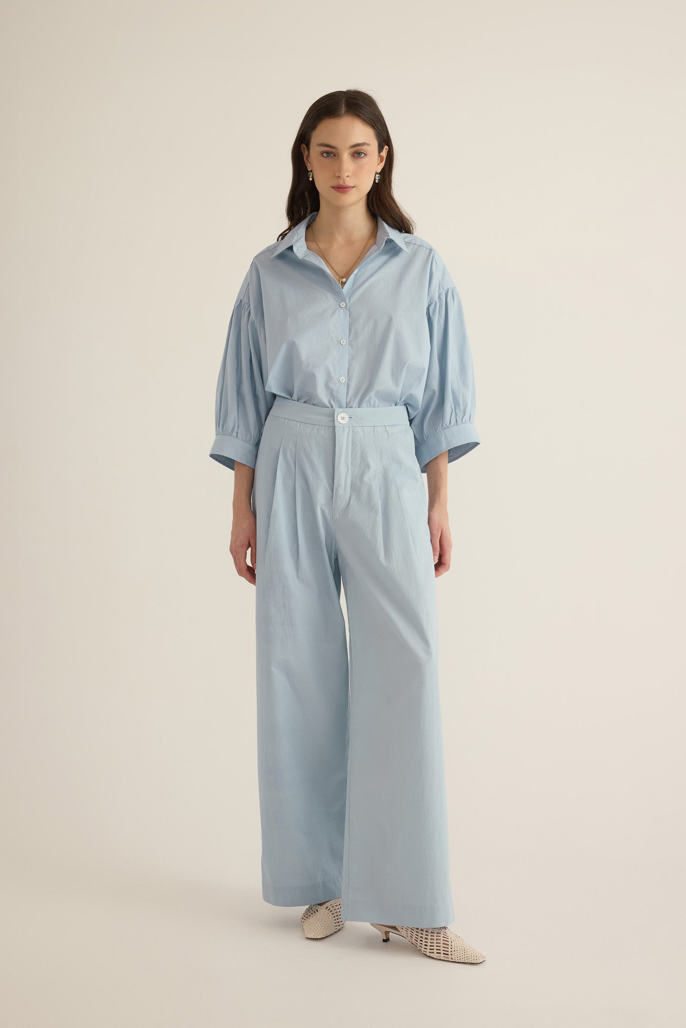 Font view of model wearing the Romeo wide-leg pleat pant in pale blue organic cotton, styled with the Romeo wide cuff blouson shirt in blue