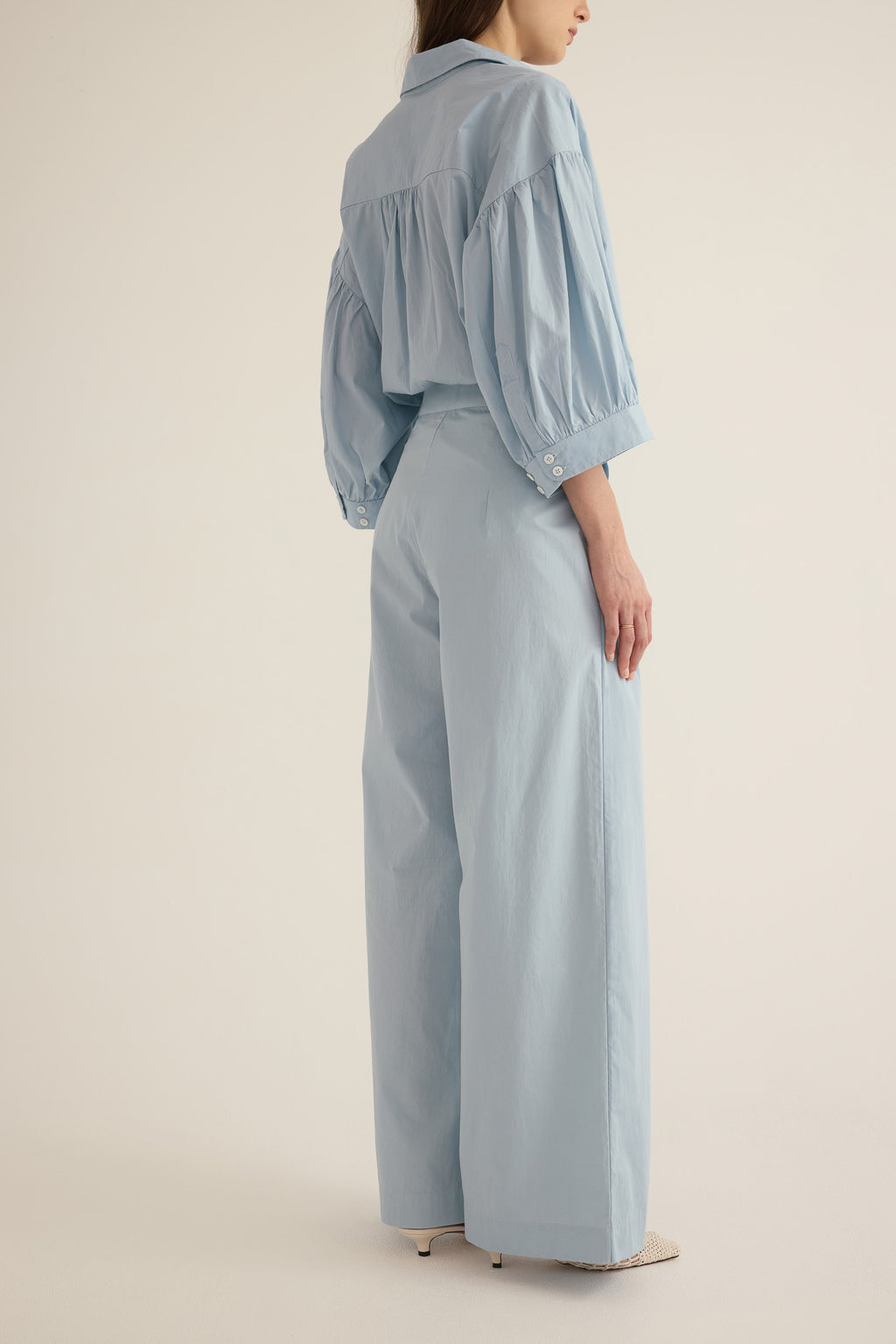 Side view of model wearing the Romeo wide-leg pleat pant in pale blue organic cotton, styled with the Romeo wide cuff blouson shirt in blue