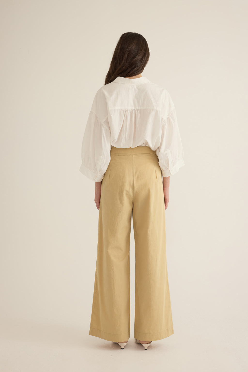 Back view of model wearing the Romeo wide-leg pleat pant in light beige organic cotton, styled with the Romeo wide cuff shirt in Ivory
