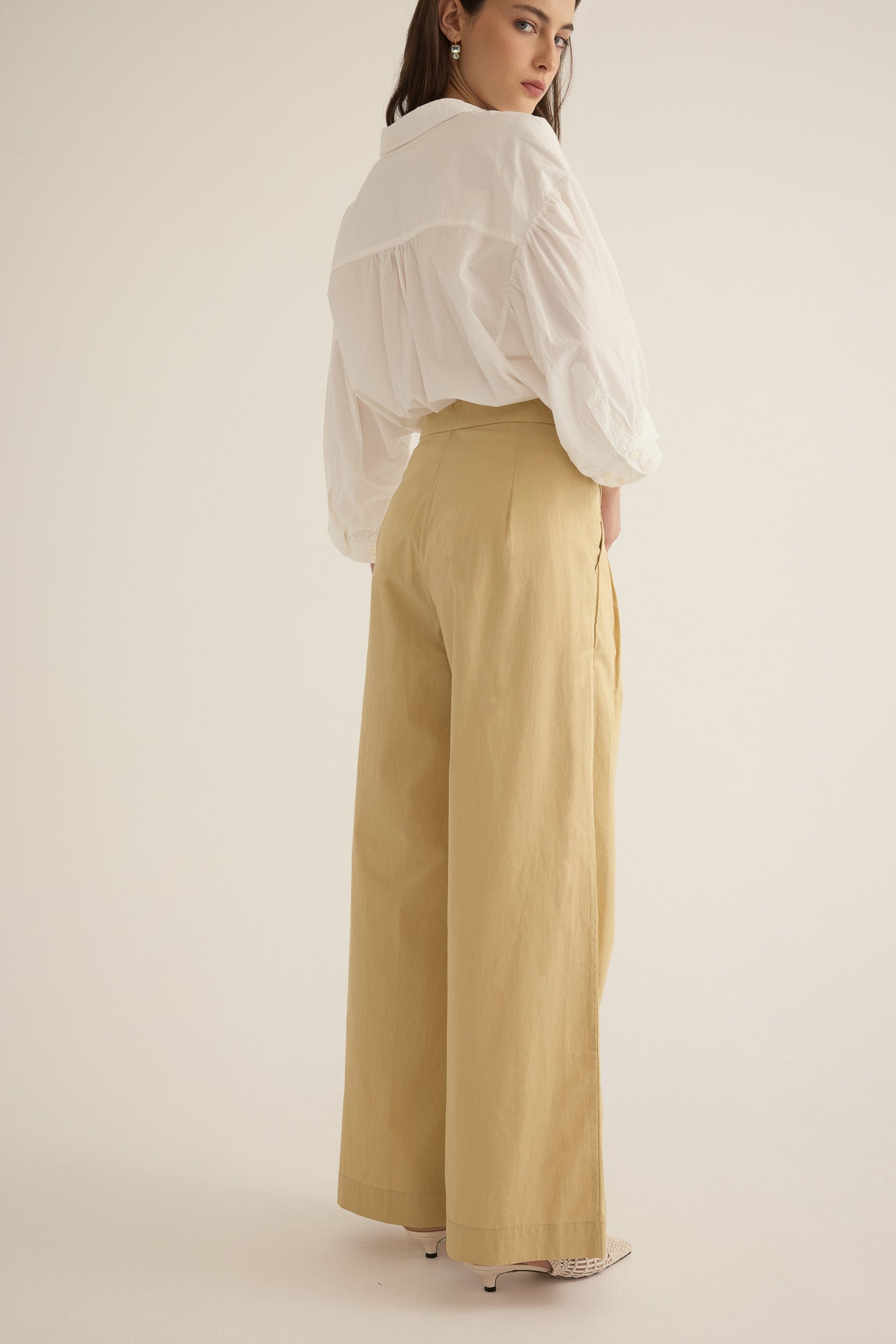 Back view of model wearing the Romeo wide-leg pleat pant in light beige organic cotton, styled with the Romeo wide cuff shirt in Ivory