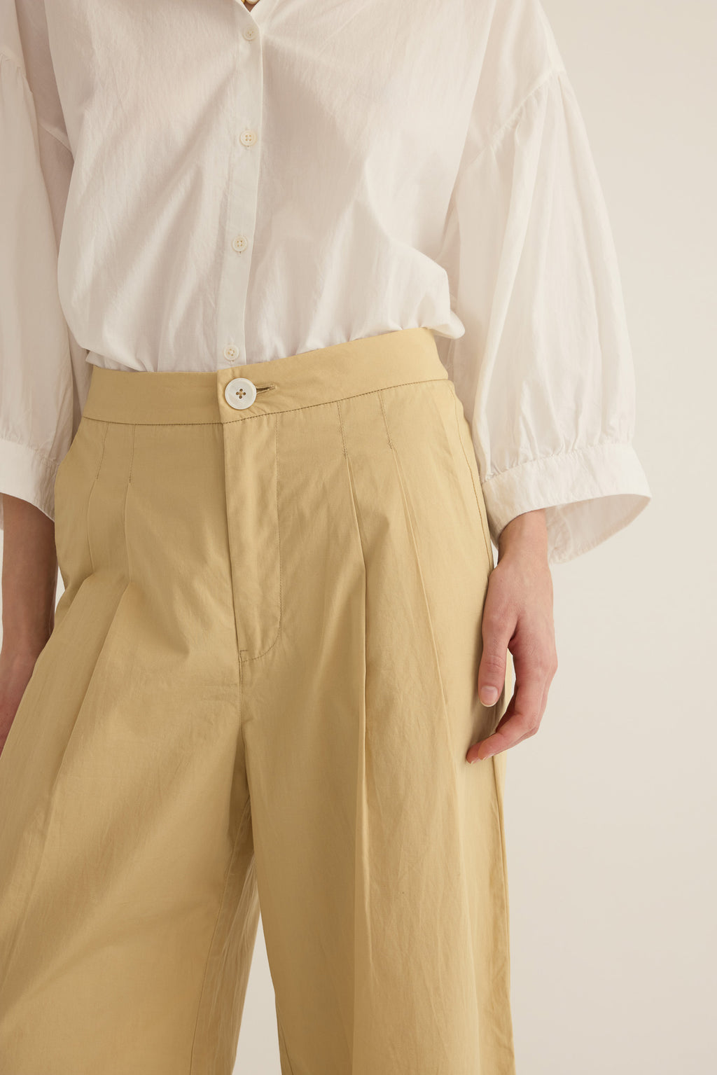 Close up of model wearing the Romeo wide-leg pleat pant in light beige organic cotton, styled with the Romeo wide cuff shirt in Ivory