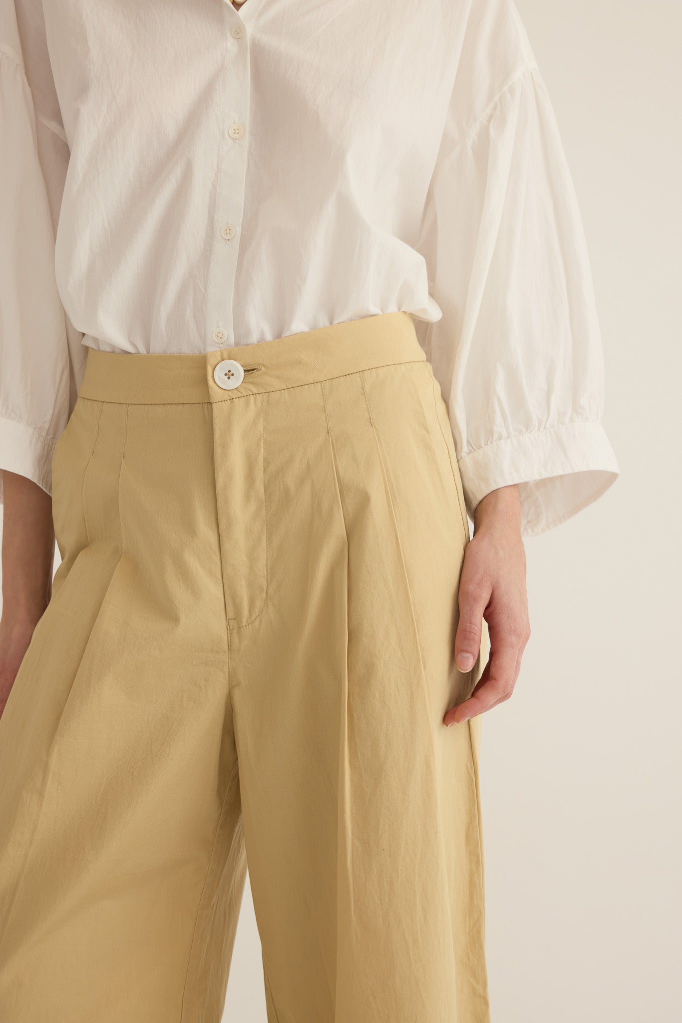 Close up of model wearing the Romeo wide-leg pleat pant in light beige organic cotton, styled with the Romeo wide cuff shirt in Ivory