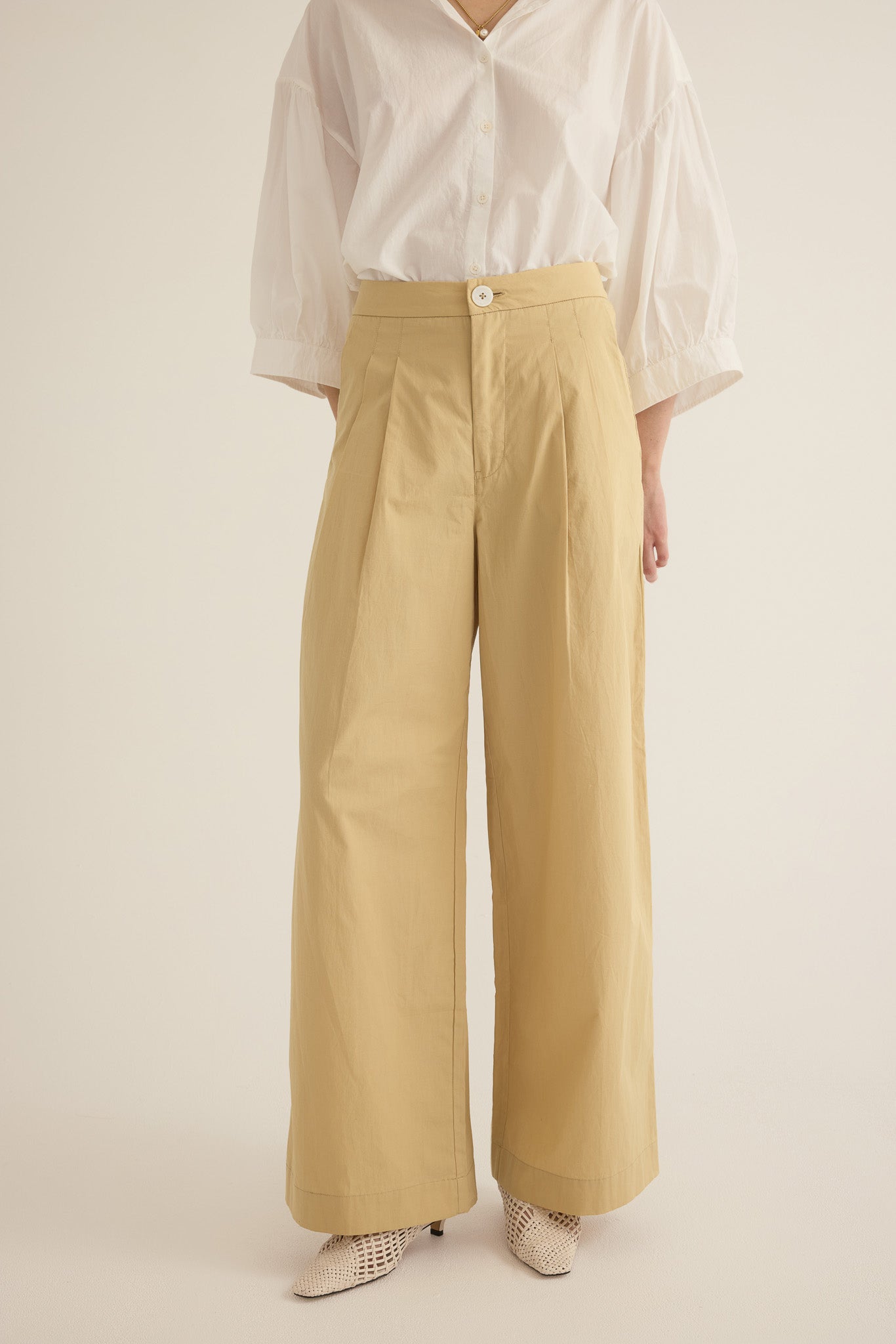 Close up of model wearing the Romeo wide-leg pleat pant in light beige organic cotton, styled with the Romeo wide cuff shirt in Ivory