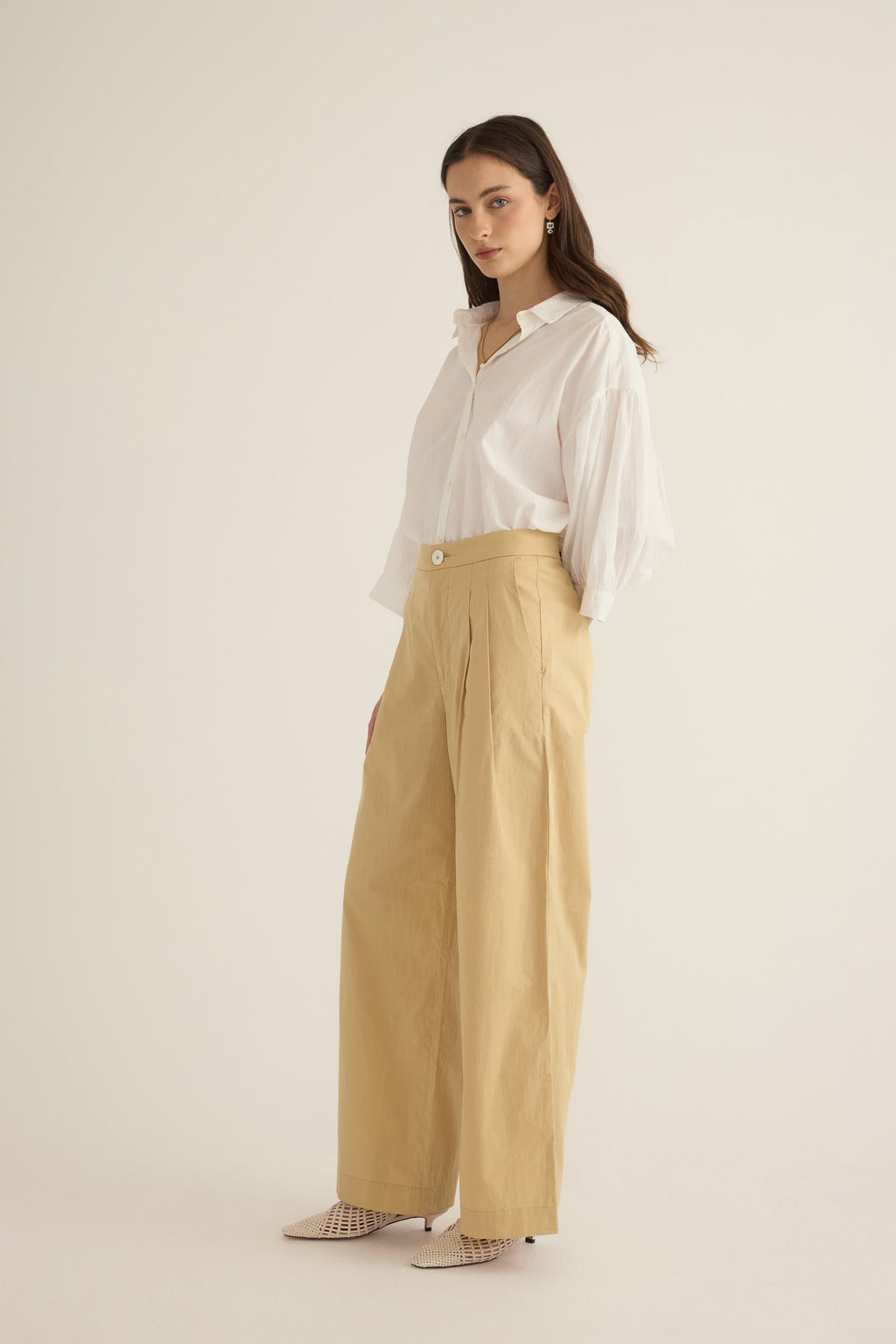 Side view of model wearing the Romeo wide-leg pleat pant in light beige organic cotton, styled with the Romeo wide cuff shirt in Ivory