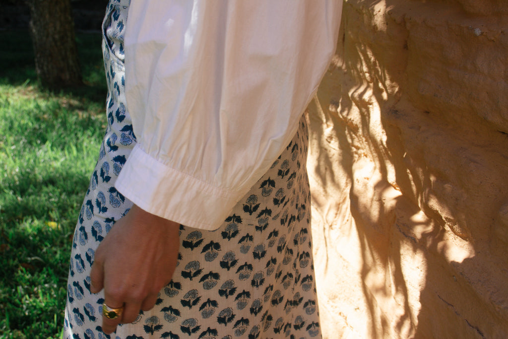 Model wearing LAYLA POET Romeo shirt in ivory white organic cotton poplin, with the handblock printed joni midi skirt, in a blue and white ditsy floral print.