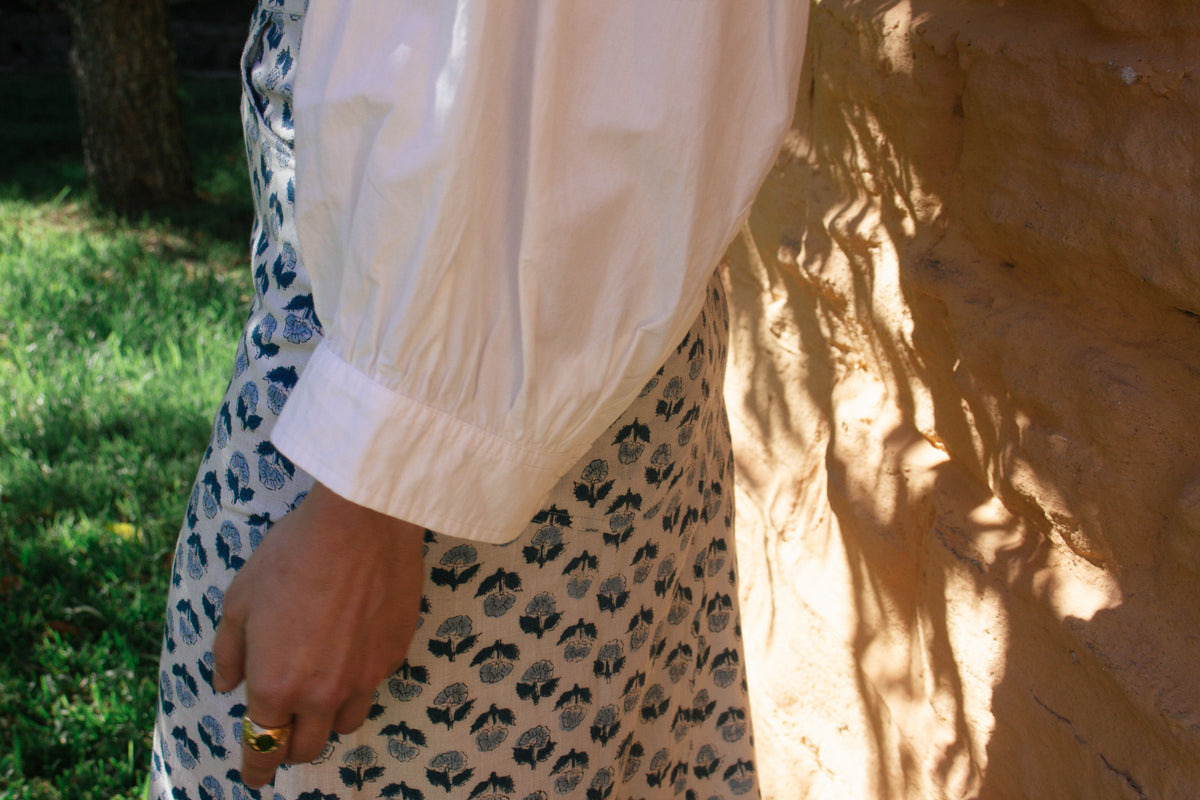 Model wearing LAYLA POET Romeo shirt in ivory white organic cotton poplin, with the handblock printed joni midi skirt, in a blue and white ditsy floral print.
